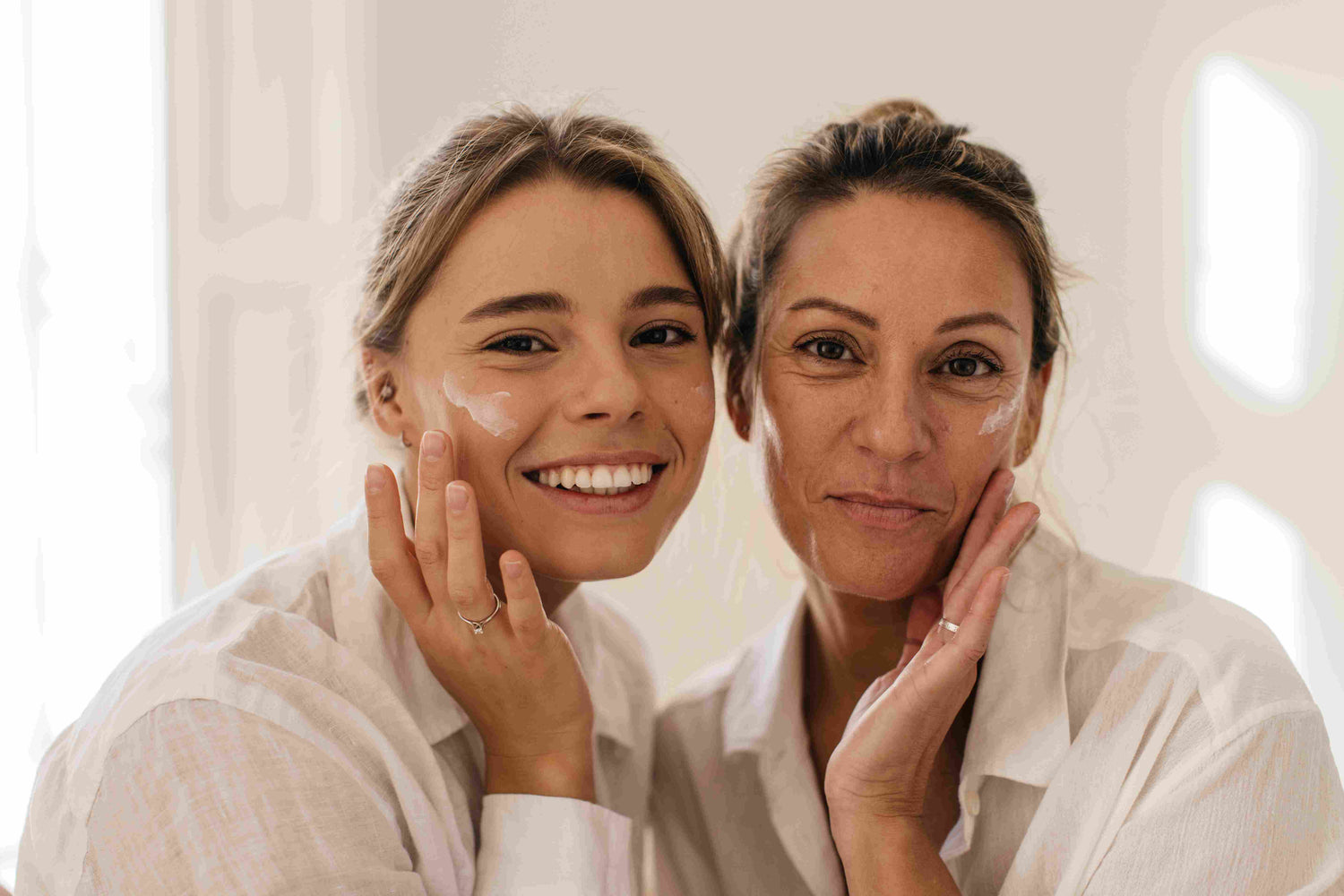 Two women smiling while applying CelaRae skincare products to their faces, embodying the brand's dedication to radiant and youthful skin.
