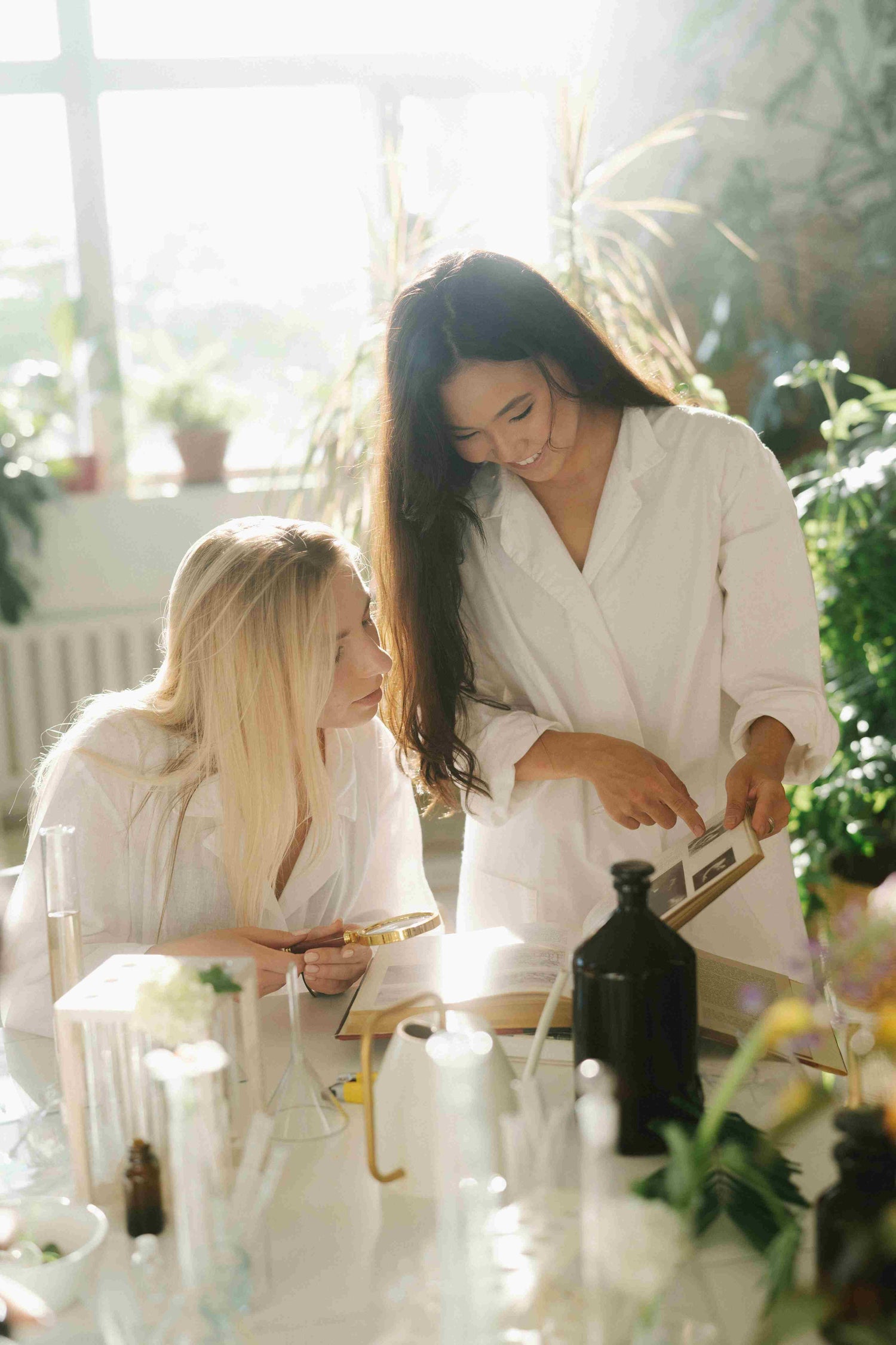 Two individuals in white robes working with skincare products in a bright, natural setting, showcasing the personalized radiant skin solutions offered by CelaRae.